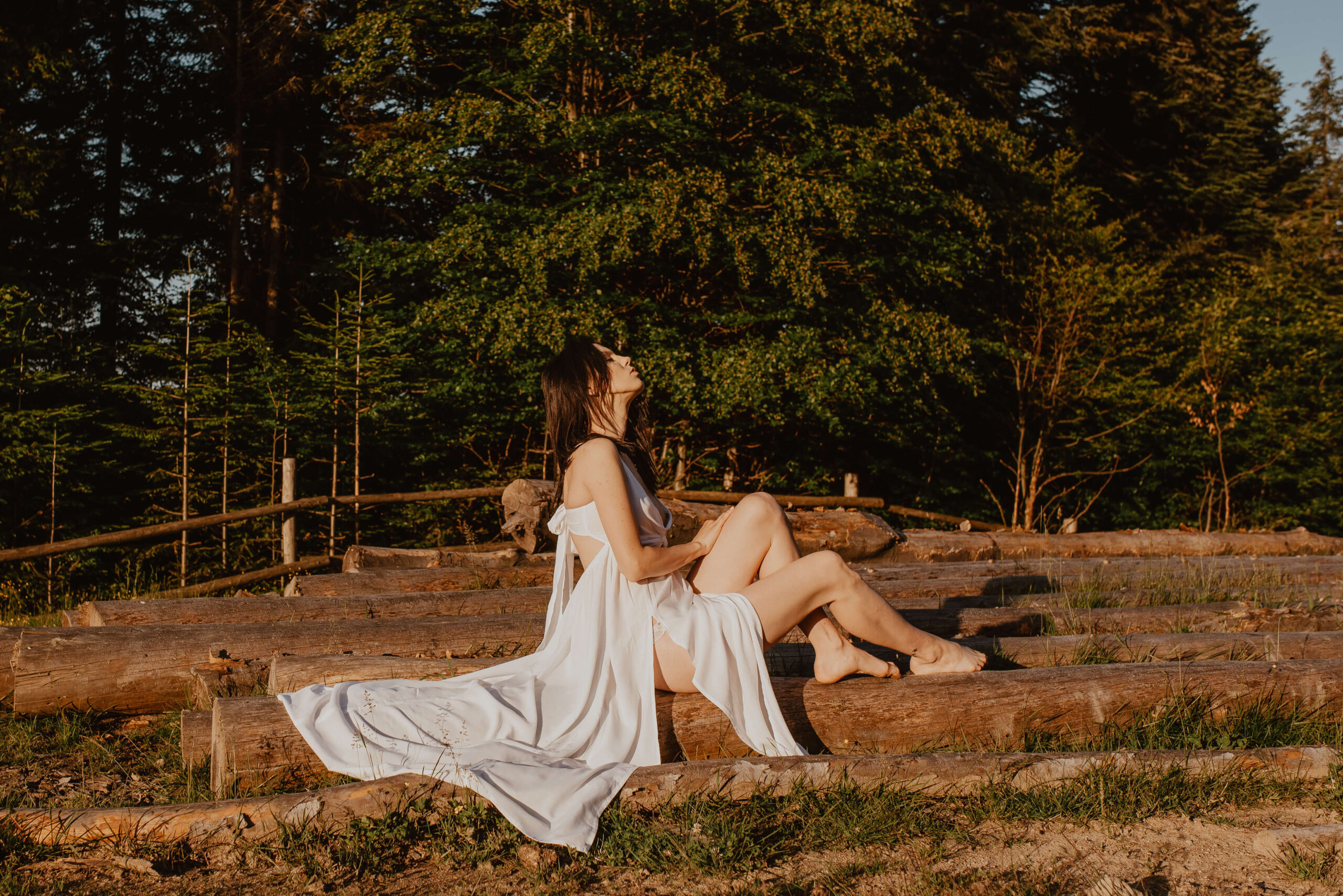 Ein Traum in Weiß! Eine wunderschöne Braut liegt auf Baumstümpfen inmitten einer Bergwiese und genießt den Sonnenaufgang. Ihr leichtes, fließendes Kleid umhüllt sie sanft und die warmen Sonnenstrahlen lassen sie erstrahlen.