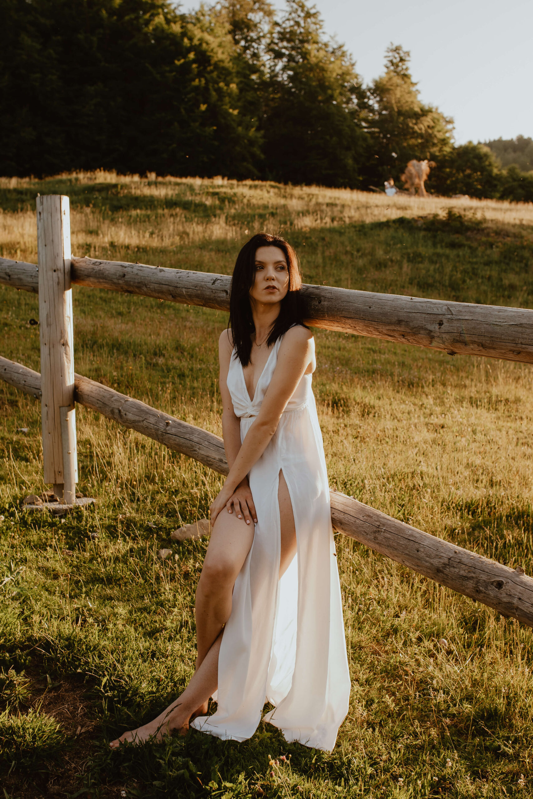 Eine bezaubernde Braut in einem zarten, fließenden Kleid, die den Sonnenaufgang in der Nähe einer rustikalen Pferdekoppel bewundert und sich von der unberührten Schönheit der Natur inspirieren lässt.