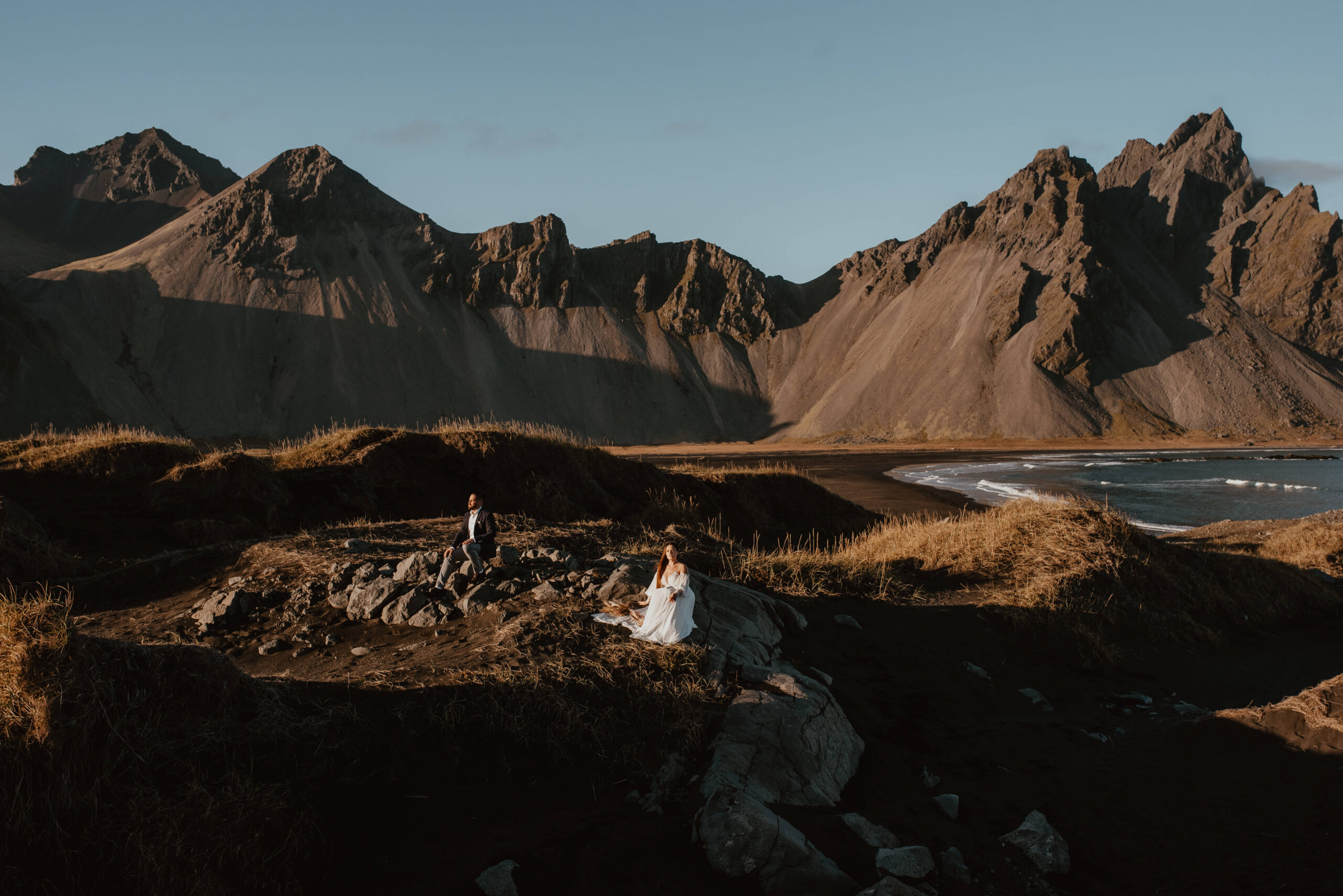 Die Fotos zeigen ein junges Brautpaar in Hochzeitskleidung auf Island an einem warmen Tag. Im Hintergrund sind die riesigen Berge und das Meer zu sehen. Das Paar klettert gemeinsam den grasbewachsenen Hügel hinauf und hält sich dabei an den Händen, während sie lachen und im Hintergrund das Rauschen der Wellen zu hören ist. Diese Szene eines Auslandshochzeitsfotoshootings erinnert an eine legendäre Szene aus dem Film "Titanic". Als Hochzeitsfotograf aus Chiemgau bin ich stolz, solche wunderschönen Momente auf Bildern festhalten zu können. Katarzyna Nord Fotografie