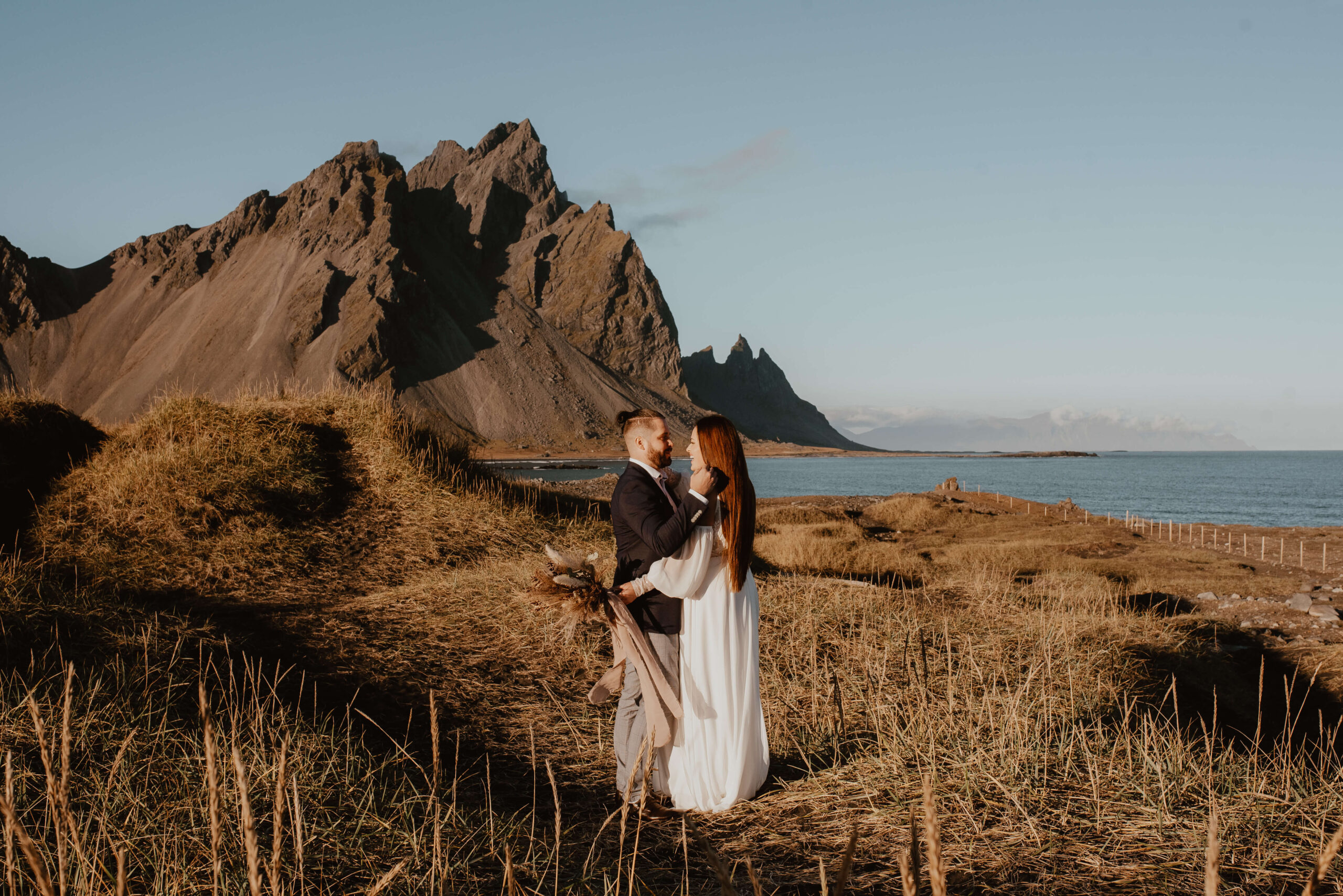 Die Fotos zeigen ein junges Paar in Hochzeitskleidung auf Island, an einem warmen Tag, im Hintergrund sieht man riesige Berge und das Meer. Das Paar schaut sich in die Augen, umarmt sich und lacht, während man im Hintergrund das Rauschen der Wellen hören kann. Diese Bilder sind der perfekte Beweis für die Schönheit und den Zauber einer Hochzeit im Ausland. Schlüsselwort: Auslandshochzeit. Katarzyna Nord Fotografie