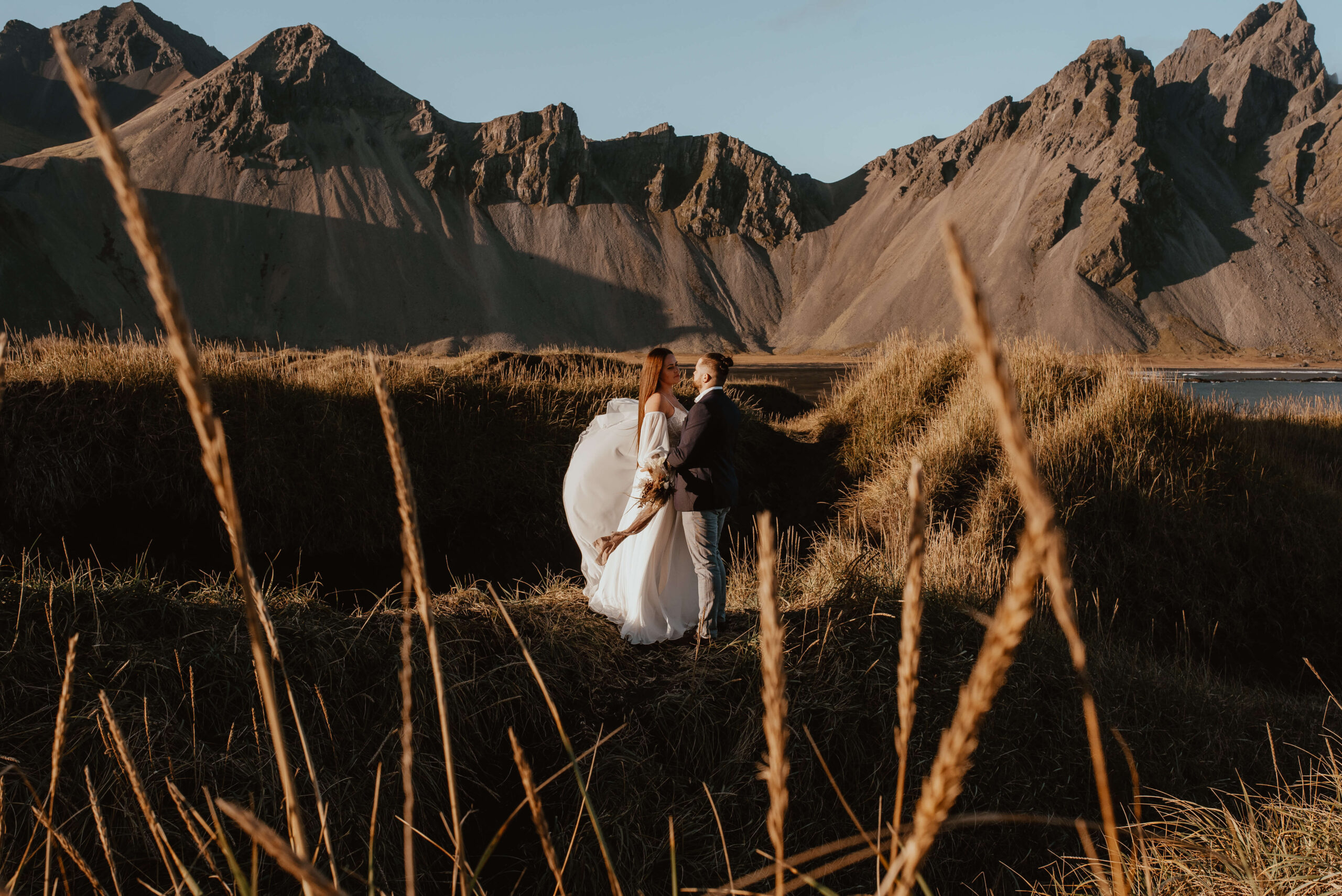 Die Fotos zeigen ein junges Paar in Hochzeitskleidung auf Island, an einem warmen Tag, im Hintergrund sieht man riesige Berge und das Meer. Das Paar schaut sich in die Augen, umarmt sich und lacht, während man im Hintergrund das Rauschen der Wellen hören kann. Diese Bilder sind der perfekte Beweis für die Schönheit und den Zauber einer Hochzeit im Ausland. Schlüsselwort: Auslandshochzeit. Katarzyna Nord fotografie