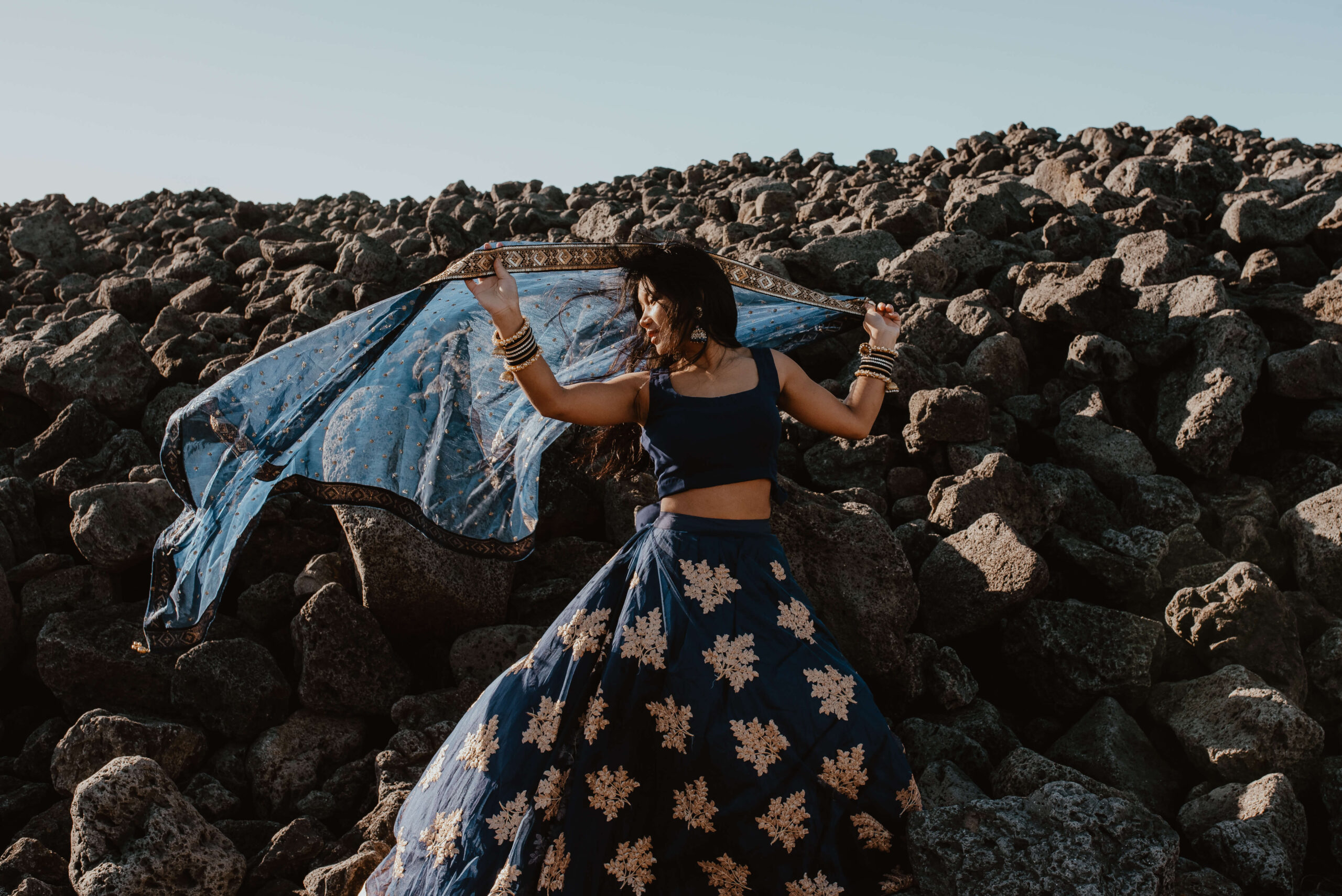 Das Foto zeigt eine junge Frau in einem traditionellen Kleid, die im Rahmen einer Fotosession an einem windigen Sommertag auf einer isländischen Wiese steht und sich in der Sonne wärmt. Die Wiese ist von grünem Gras bedeckt und im Hintergrund sind majestätische Berge und Hügel zu sehen. Die Farben des Fotos sind überwiegend Grün- und Blautöne, die die Schönheit und Unberührtheit der isländischen Landschaft widerspiegeln. Die junge Frau steht in einer selbstbewussten Haltung da und verleiht dem Foto eine gewisse Stärke und Entschlossenheit. In ihrer traditionellen Kleidung zeigt sie eine Verbindung zu ihrer Heimat und kulturellen Identität. Das Foto ist Teil einer Fotosession, die speziell für Frauen konzipiert wurde. Das Ziel ist es, die Schönheit und Stärke von Frauen in verschiedenen Kulturen und Ländern zu feiern. In diesem Kontext unterstreicht das Foto die Schönheit und Stärke isländischer Frauen und ihre tiefe Verbindung zur Natur. Insgesamt ist das Foto ein beeindruckendes Porträt einer jungen Frau, das in einer speziell für Frauen konzipierten Fotosession entstanden ist.